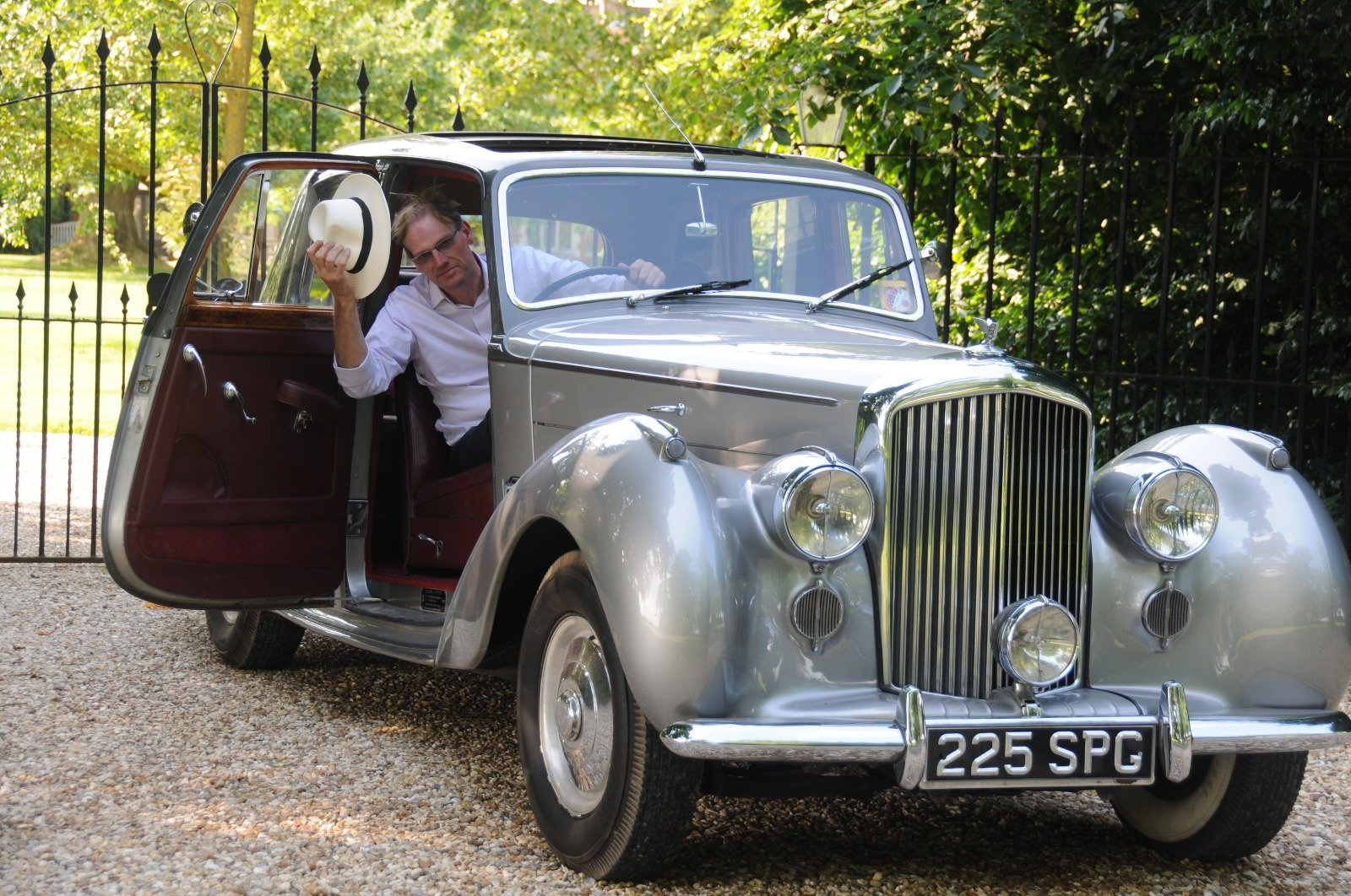 Dimitri Labis stepping out of a silver 1950s Bentley, panama hat in hand
